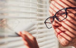 Curious man with eyeglasses looking through a jalousie. Themes curiousity, surveillance or eyesight.